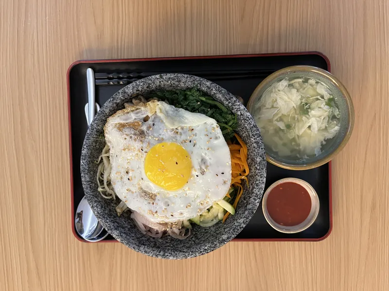 Dolsot bibimbap with a fried egg, soup and side dishes on a black tray